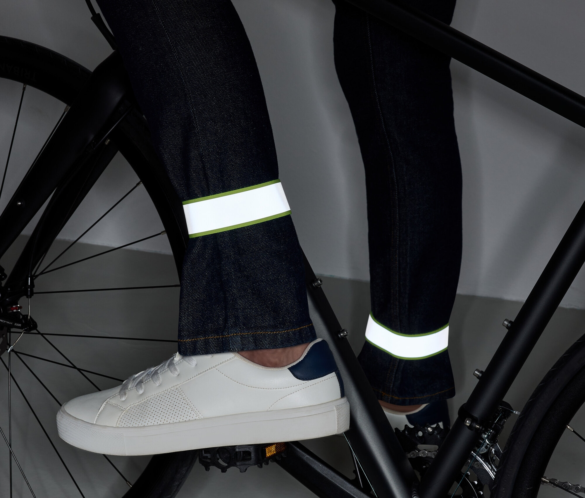 Jambes sur un vélo en jean avec des bandes réfléchissantes et des chaussures blanches.