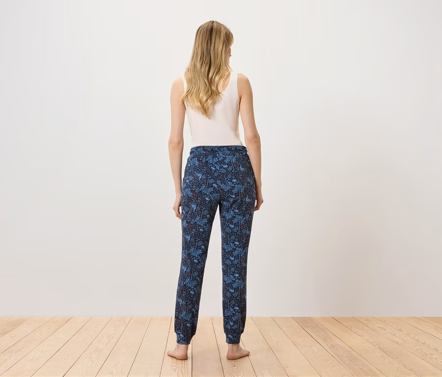 Une femme, vue de dos, porte un débardeur blanc et un pantalon bleu imprimé.