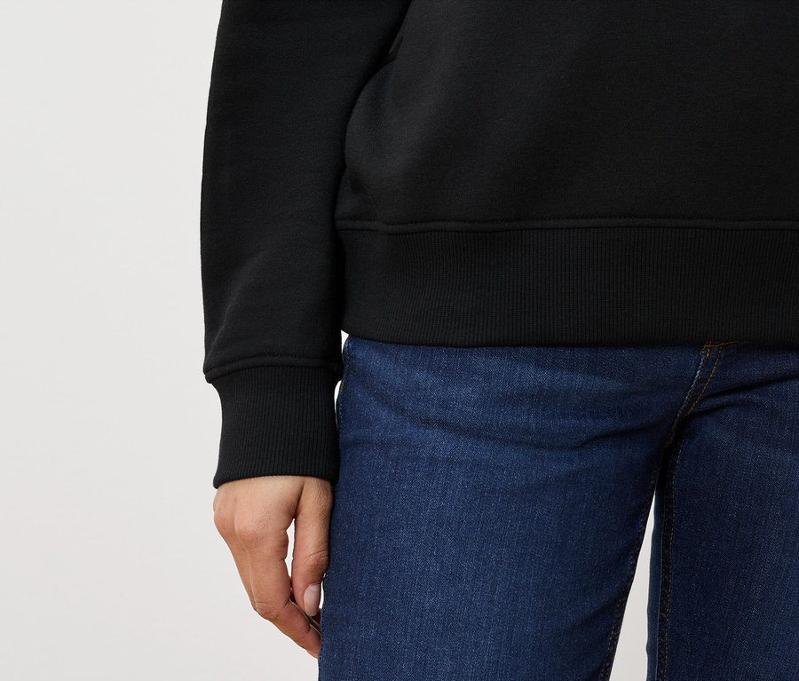 Vue partielle d'une personne portant un pull noir et un jean bleu.