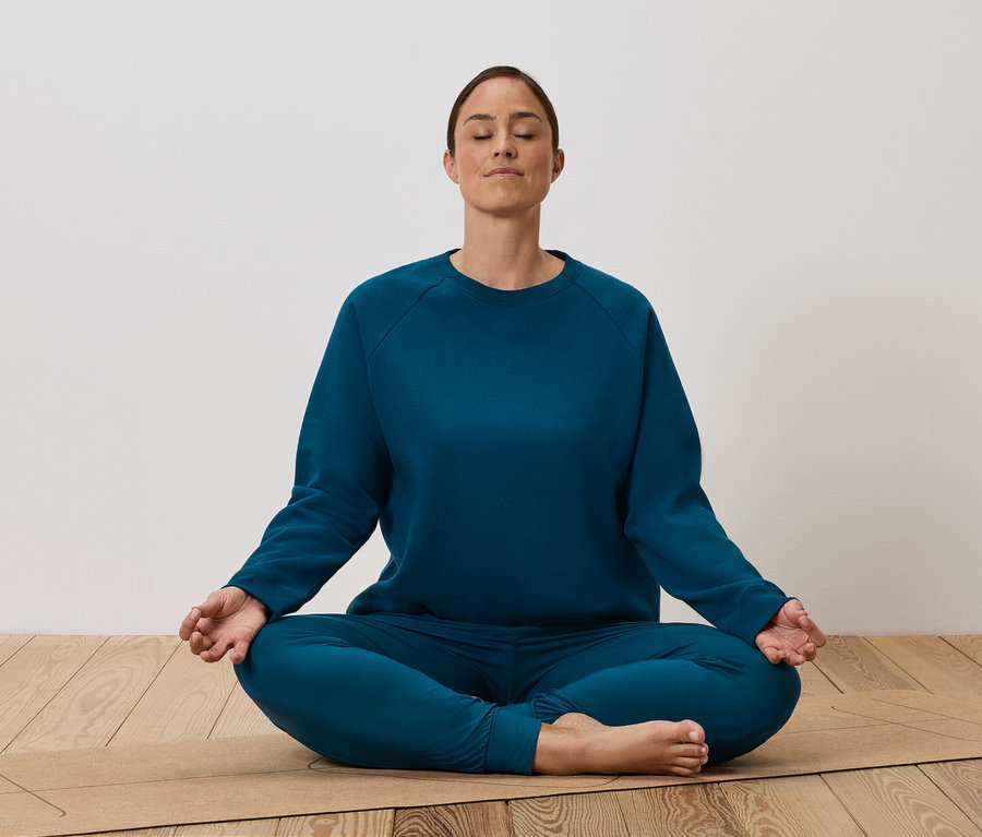 Une femme est assise en tailleur sur un tapis de yoga et médite.