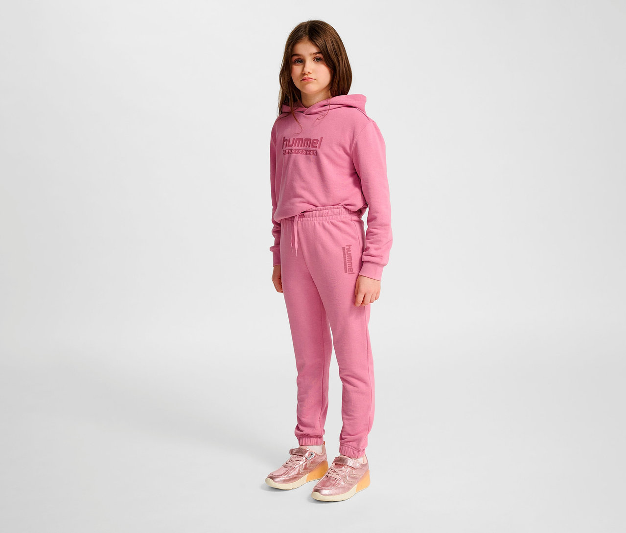 Une fille portant un pantalon régulier HUMMEL HMLJR Base rose et un sweat à capuche.
