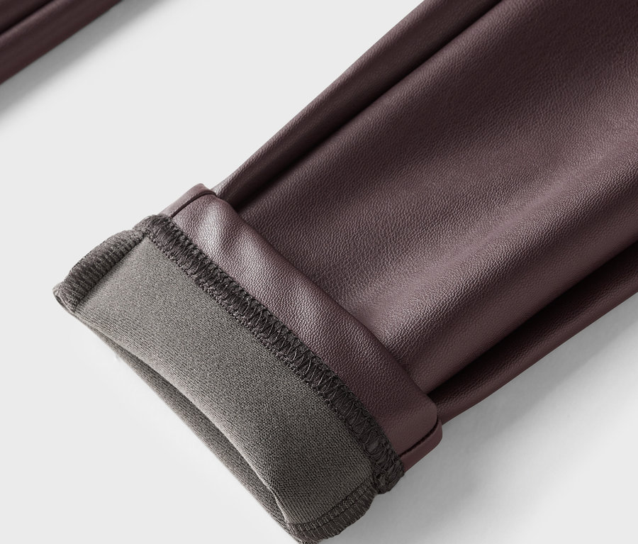 Gros plan sur un pantalon en cuir marron avec un ourlet retroussé et une doublure grise.