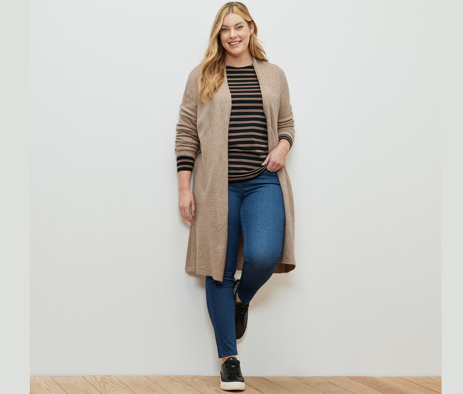 Femme posant en jegging, un haut manches longues à rayures noir et marron et un cardigan long ouvert.