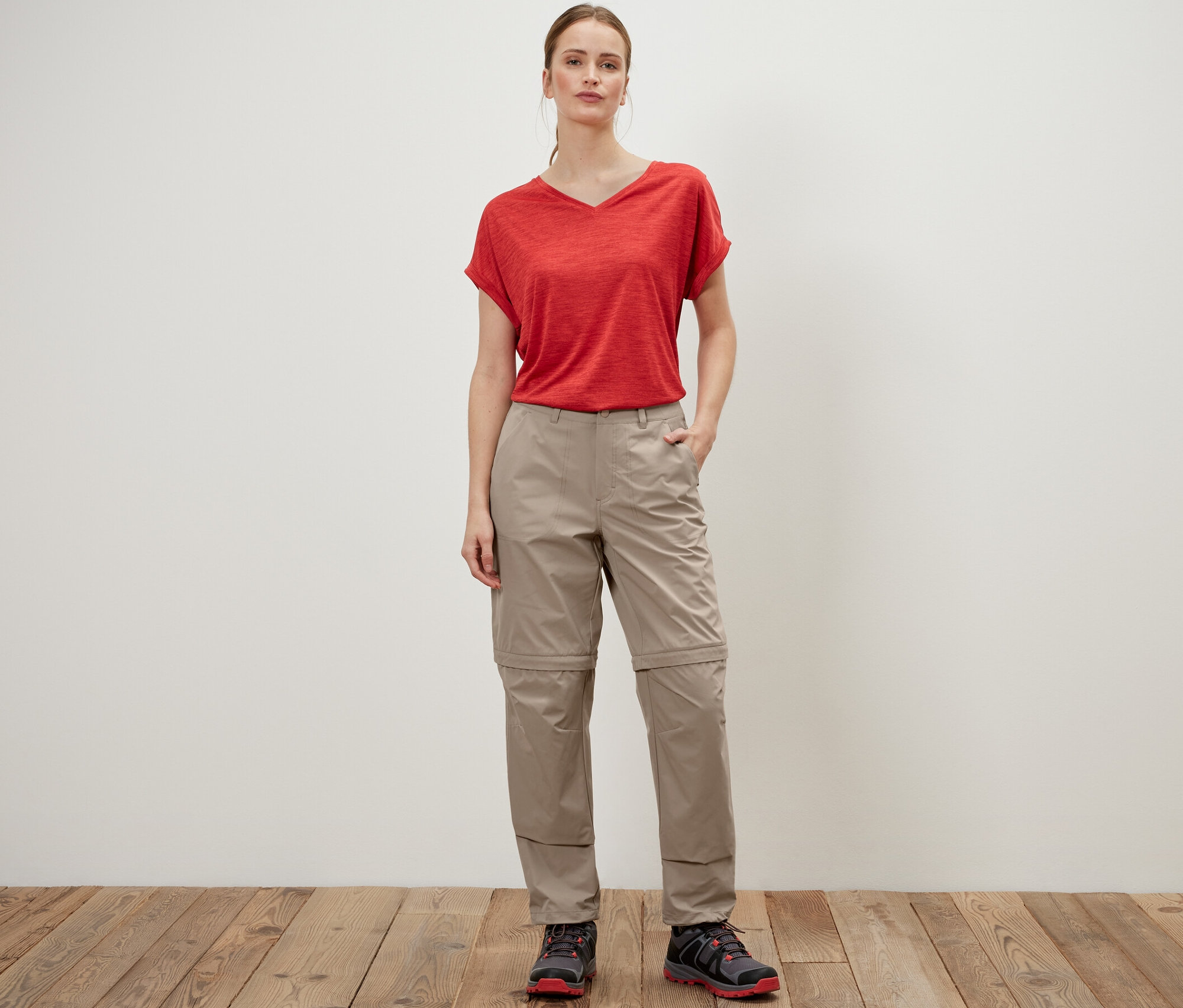Une femme pose en pantalon fonctionnel 2 en 1 beige et un t-shirt rouge.
