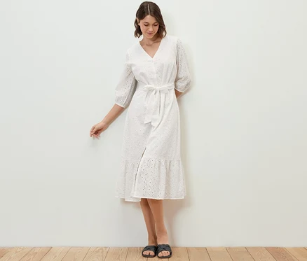Une femme debout porte une robe avec broderie ajourée.