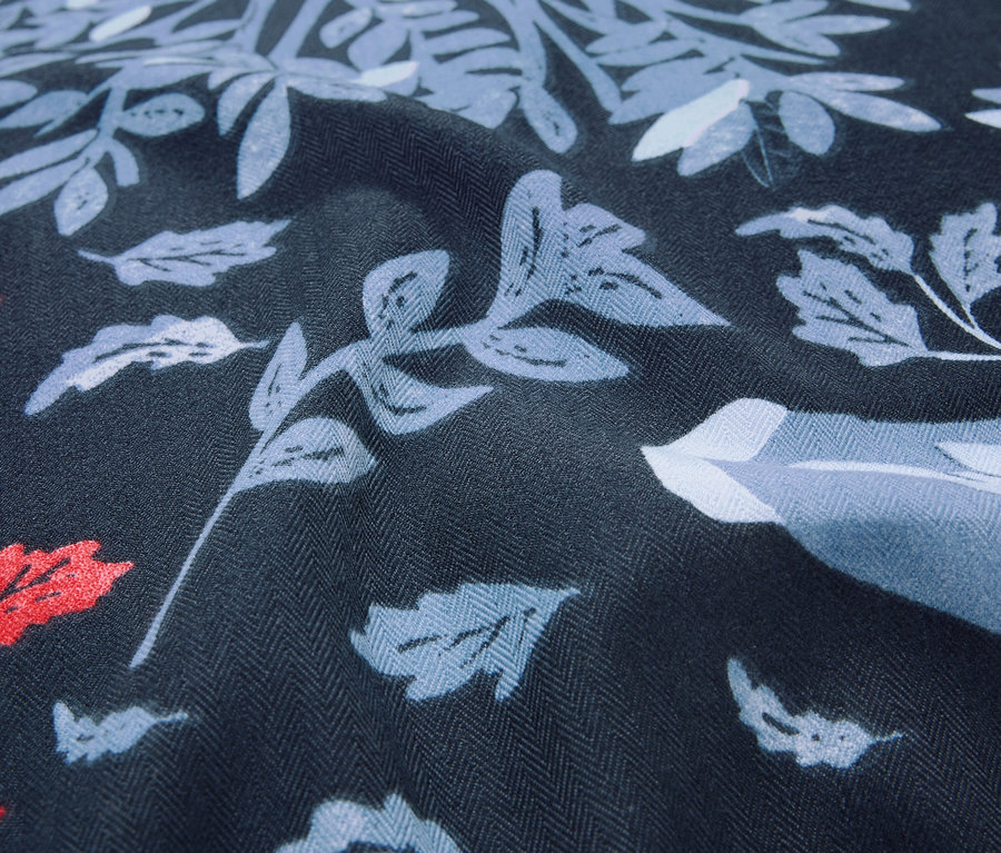 Gros plan d'un tissu bleu foncé avec un motif de feuilles et de fleurs dans les tons de bleu et de rouge.