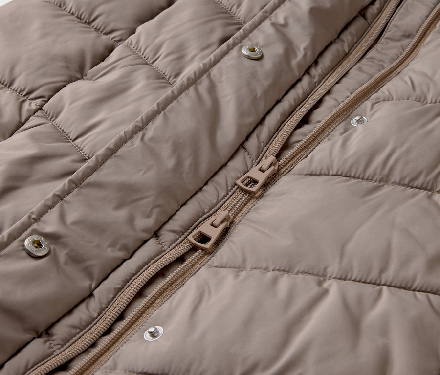 Détail d'une doudoune beige avec fermeture éclair et boutons-pression.