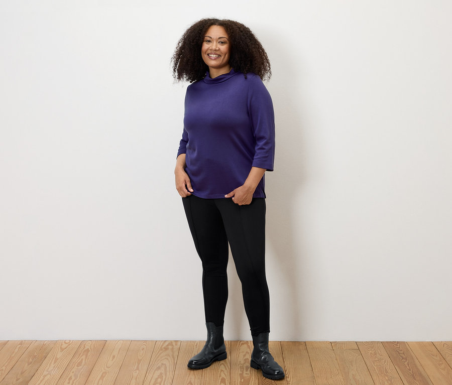 Femme posant en leggings épais noirs avec liseré et haut violet.