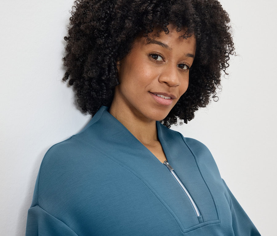 Portrait d'une femme souriante avec une coiffure afro portant un sweat-shirt bleu-vert à fermeture éclair.