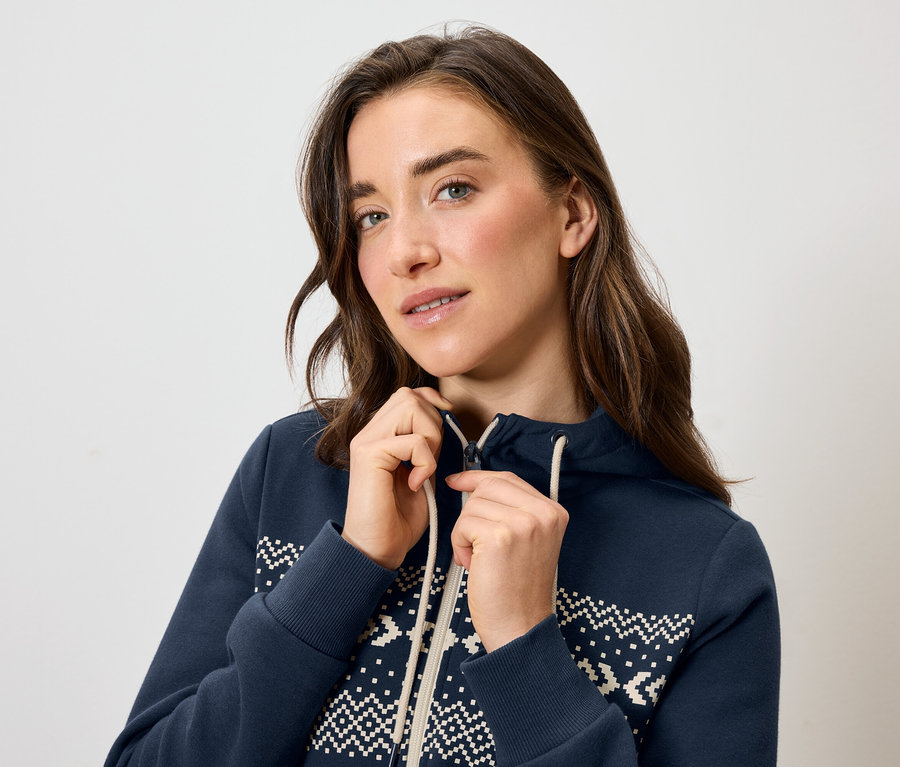 Une femme ferme une veste à capuche bleue avec un motif blanc.