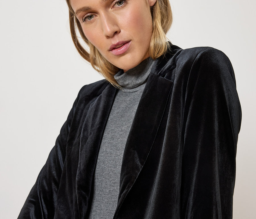 Une femme portant un blazer en velours noir et un col roulé gris.