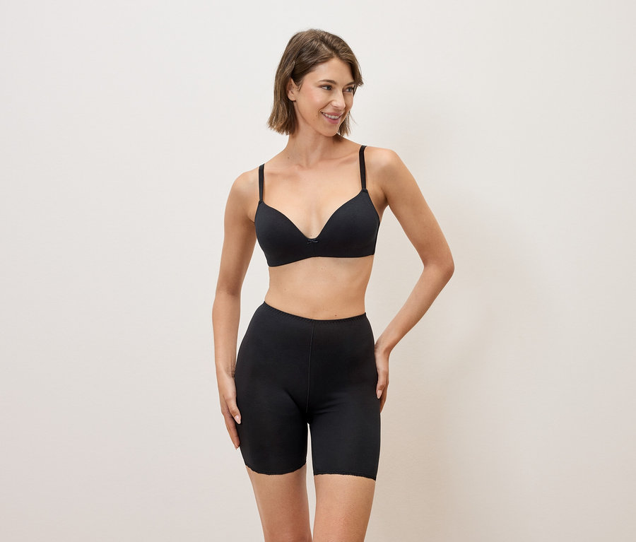 Une femme portant un soutien-gorge noir et un short noir pose sur un fond neutre.