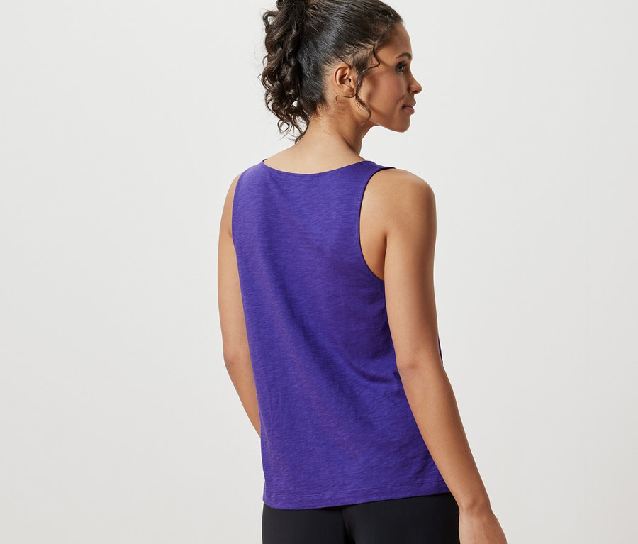 Une femme vue de dos porte un haut violet en mélange modal et un pantalon noir.