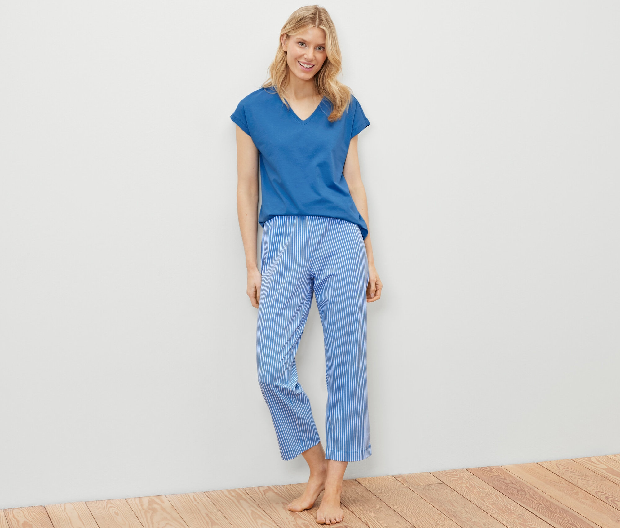 Une femme blonde est debout et porte un ensemble pyjama composé d'un t-shirt bleu et d'un pantalon rayé bleu et blanc.