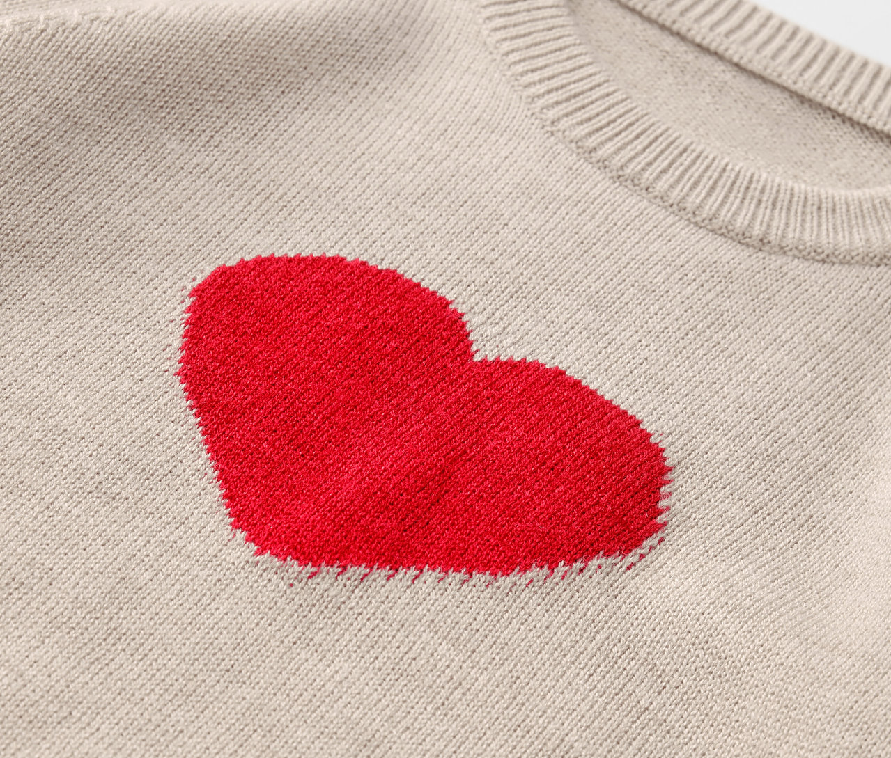 Gros plan d'un pull beige avec un cœur rouge.