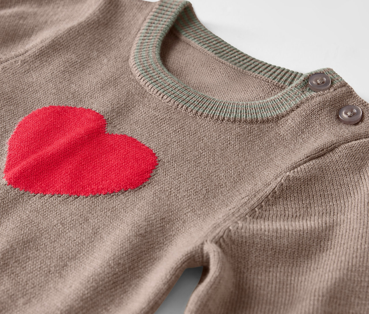 Gros plan d'un pull marron avec un cœur rouge sur le devant et des boutons sur l'épaule.