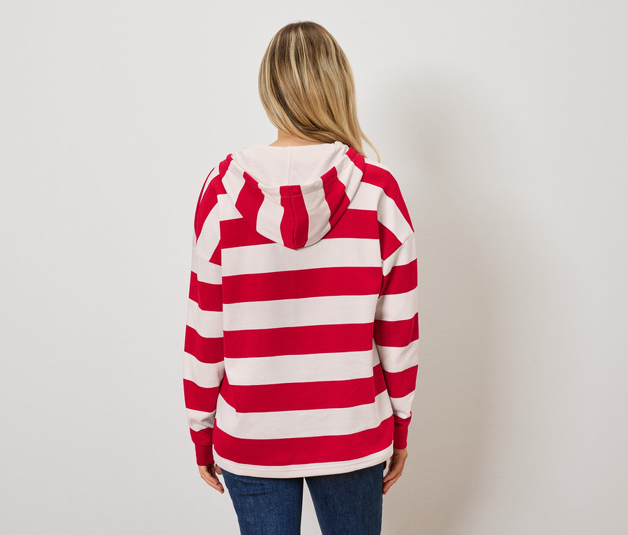 Une femme, dos à la caméra, porte un sweat à capuche rayé rouge et blanc et un jean bleu.