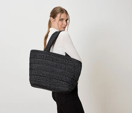 Femme portant un grand sac fourre-tout matelassé à motif léopard sur l'épaule.