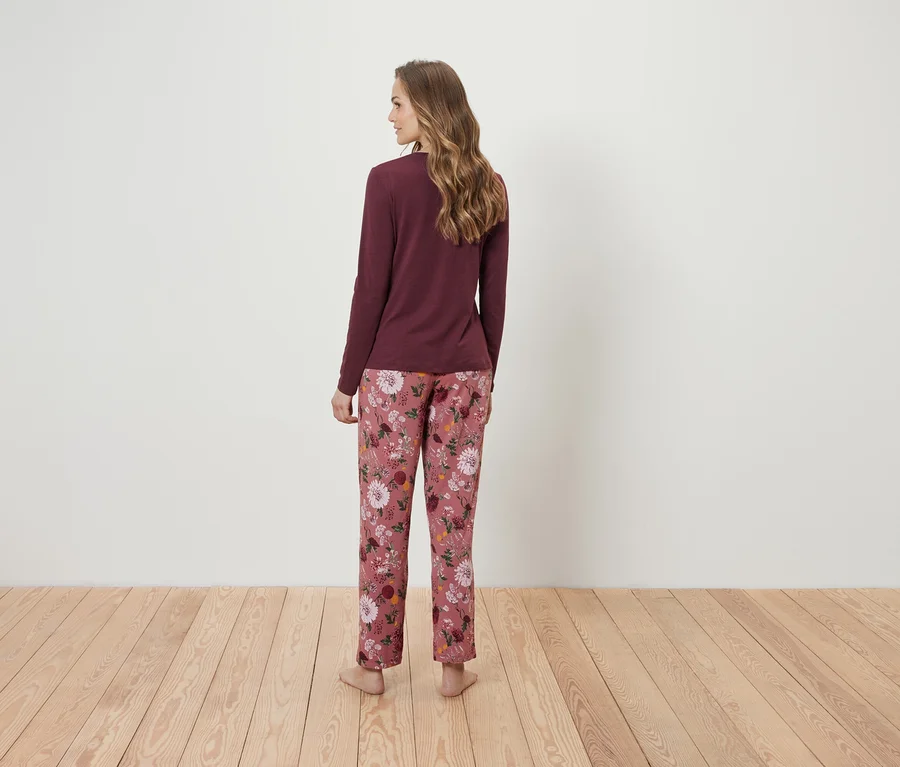 Femme vue de dos portant un t-shirt à manches longues bordeaux et un pantalon de pyjama rose à fleurs.