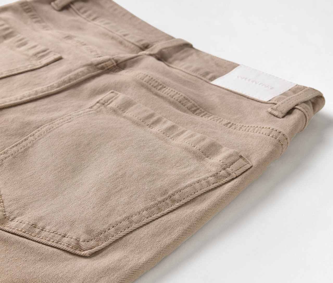 Gros plan sur un jean beige avec poches et patch logo.