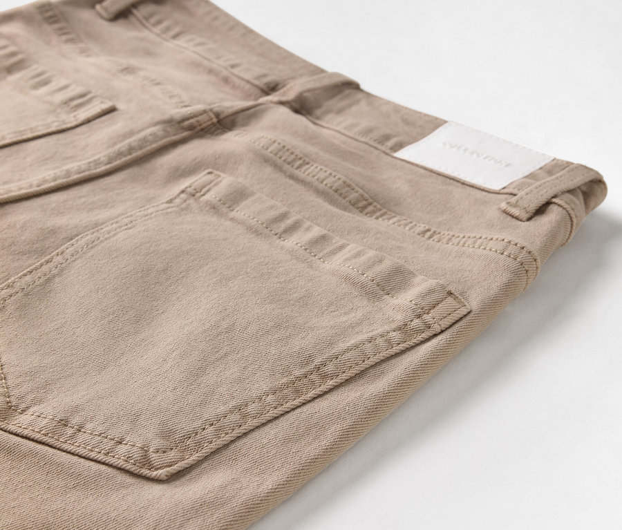 Gros plan sur un jean beige avec poches et patch logo.