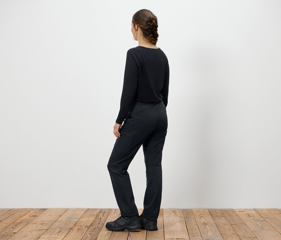 Femme en pull noir et pantalon debout, dos à la caméra.