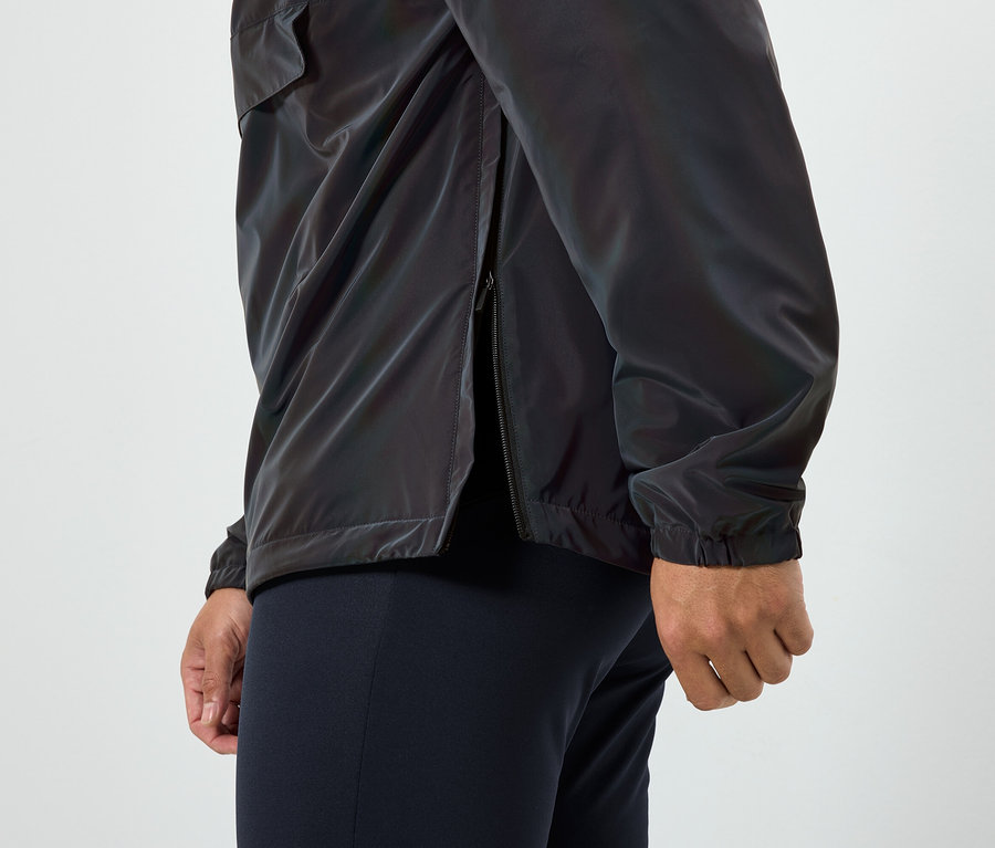 Un homme porte une veste brillante avec une fermeture éclair ouverte sur le côté et un pantalon bleu foncé.