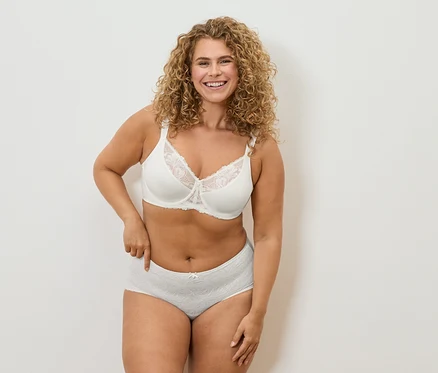 Femme souriante aux cheveux bouclés portant un soutien-gorge en dentelle blanc et une culotte grise.