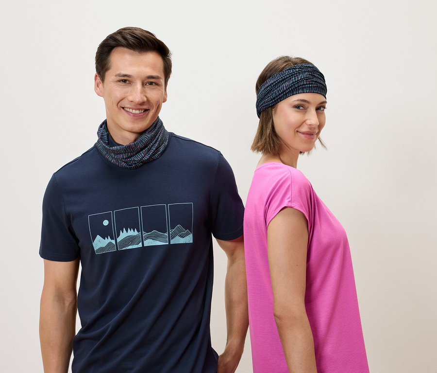 Un homme portant un t-shirt bleu marine et un cache-cou et une femme portant un bandeau et un t-shirt rose se tiennent dos à dos devant un fond blanc.