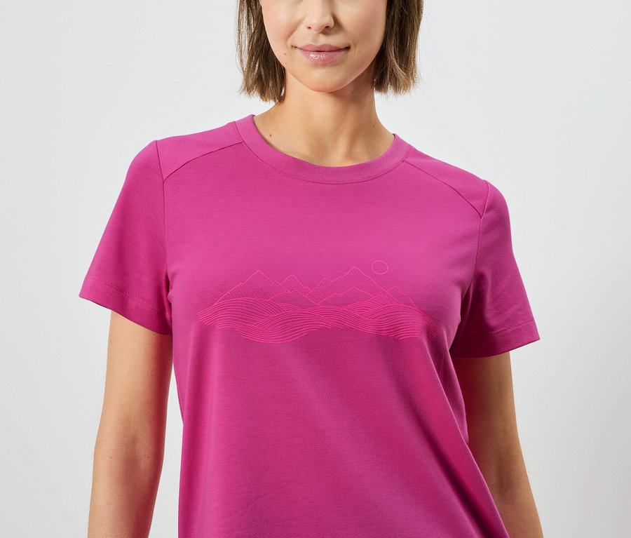 Une femme porte un t-shirt rose avec un paysage de montagne.