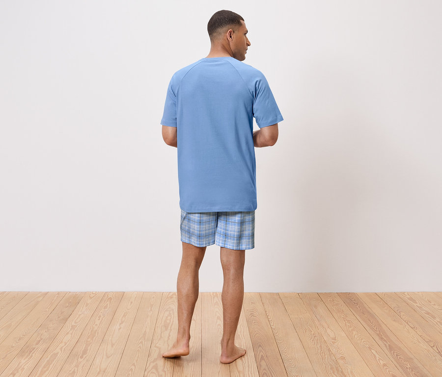Un homme vu de dos porte un t-shirt de pyjama bleu et un short à carreaux.