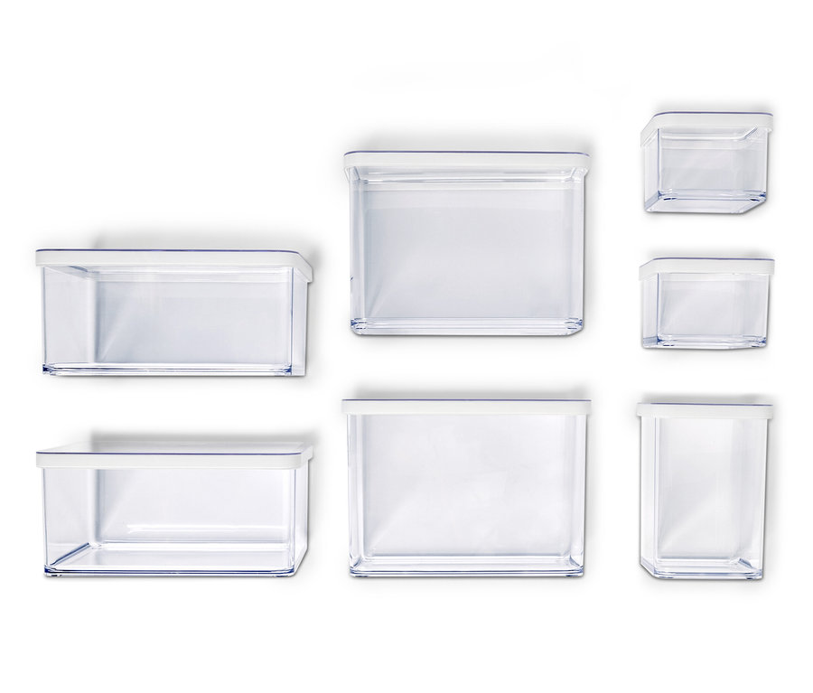 Sept récipients de rangement vides et transparents avec des couvercles blancs de différentes tailles disposés sur un fond blanc.