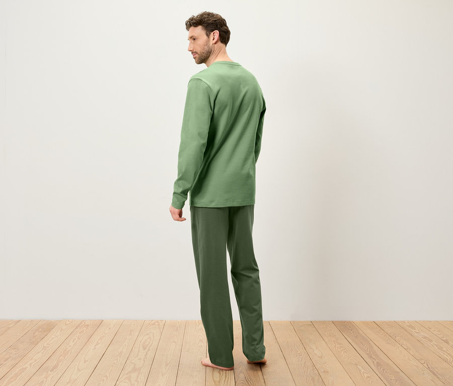 Un homme se tient dos à l'appareil photo, vêtu d'un pyjama vert sur un plancher en bois.
