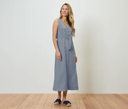 Femme debout dans une robe rayée bleu et blanc et des sandales bleues.