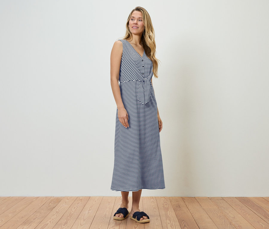 Femme debout dans une robe rayée bleu et blanc et des sandales bleues.