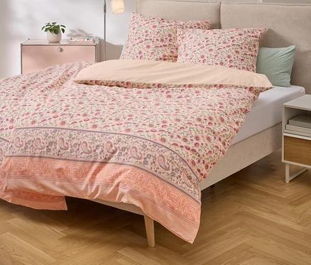 Lit avec des draps à motifs floraux roses et des oreillers assortis sur un plancher de bois.