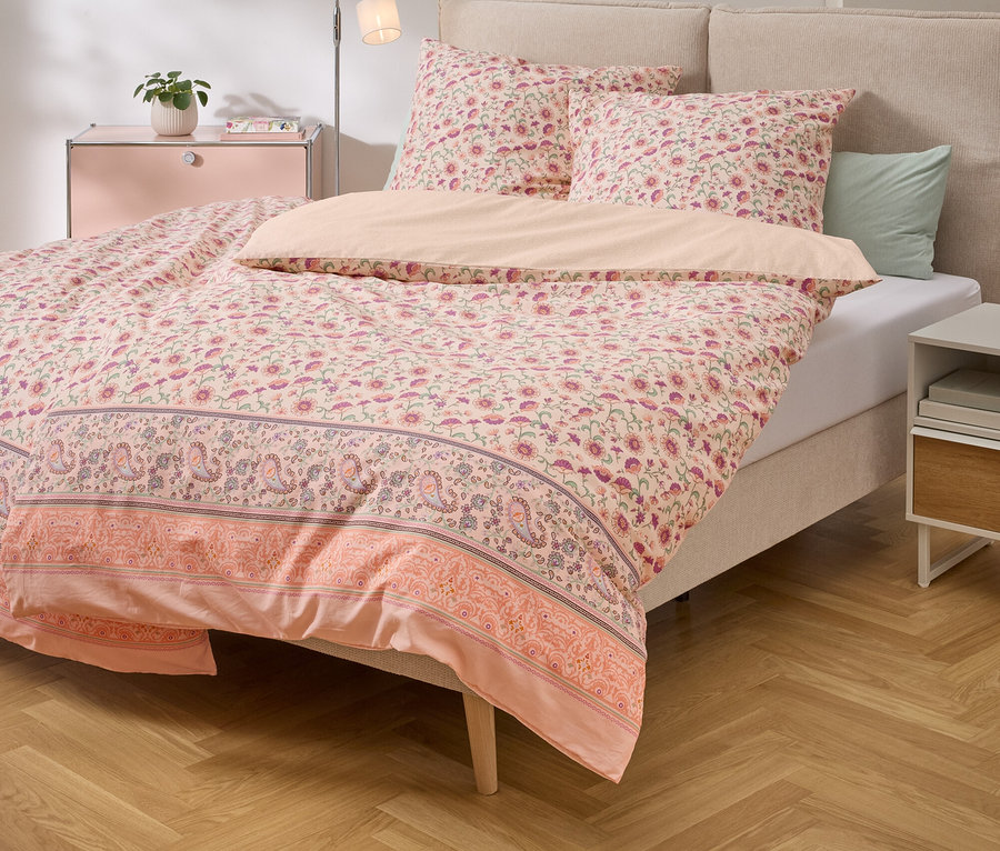 Lit avec des draps à motifs floraux roses et des oreillers assortis sur un plancher de bois.
