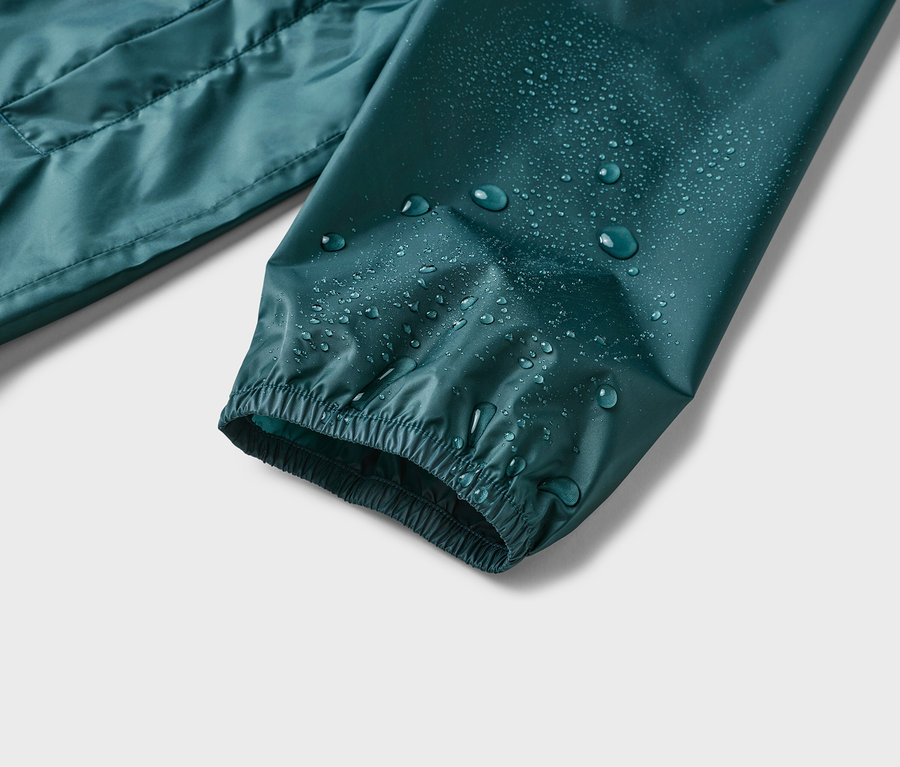 Gros plan sur la manche d'une veste imperméable vert foncé avec des gouttes d'eau dessus.