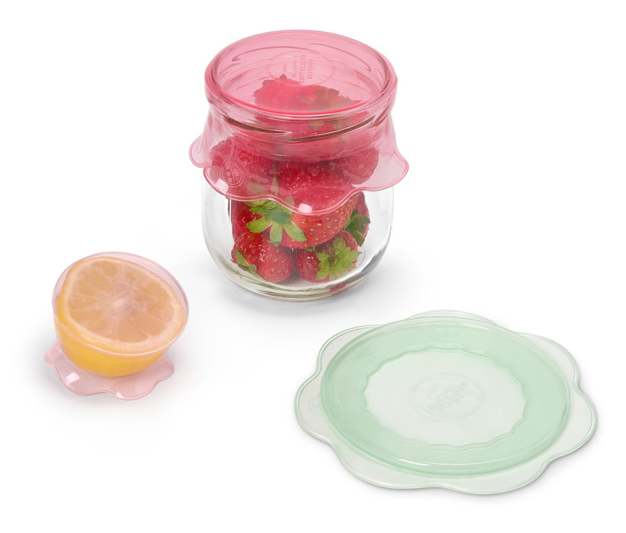 Un pot de fraises avec un couvercle rose à côté d'un demi-citron avec un couvercle rose et un couvercle vert.