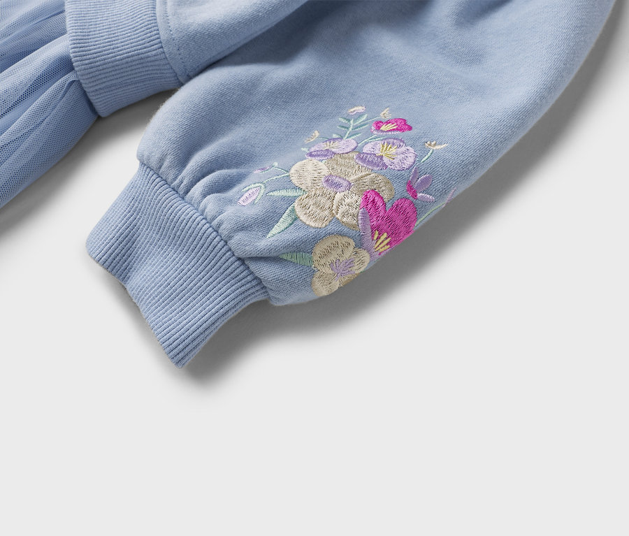 Gros plan sur un sweat-shirt bleu clair avec une broderie florale sur la manche et un bord-côtes.