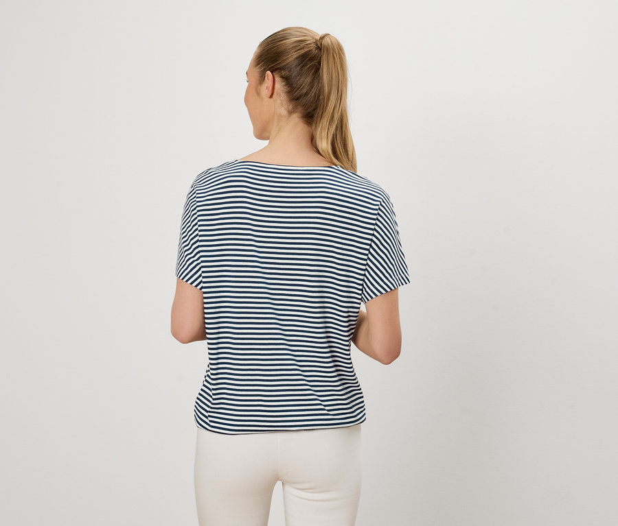 Femme avec queue de cheval blonde portant un t-shirt rayé bleu et blanc et un pantalon clair, vue de dos.