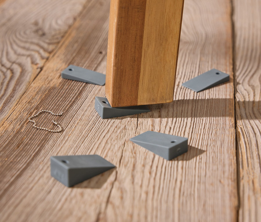 Un pied de table repose sur un plancher en bois, avec des cales grises utilisées pour la stabilisation.