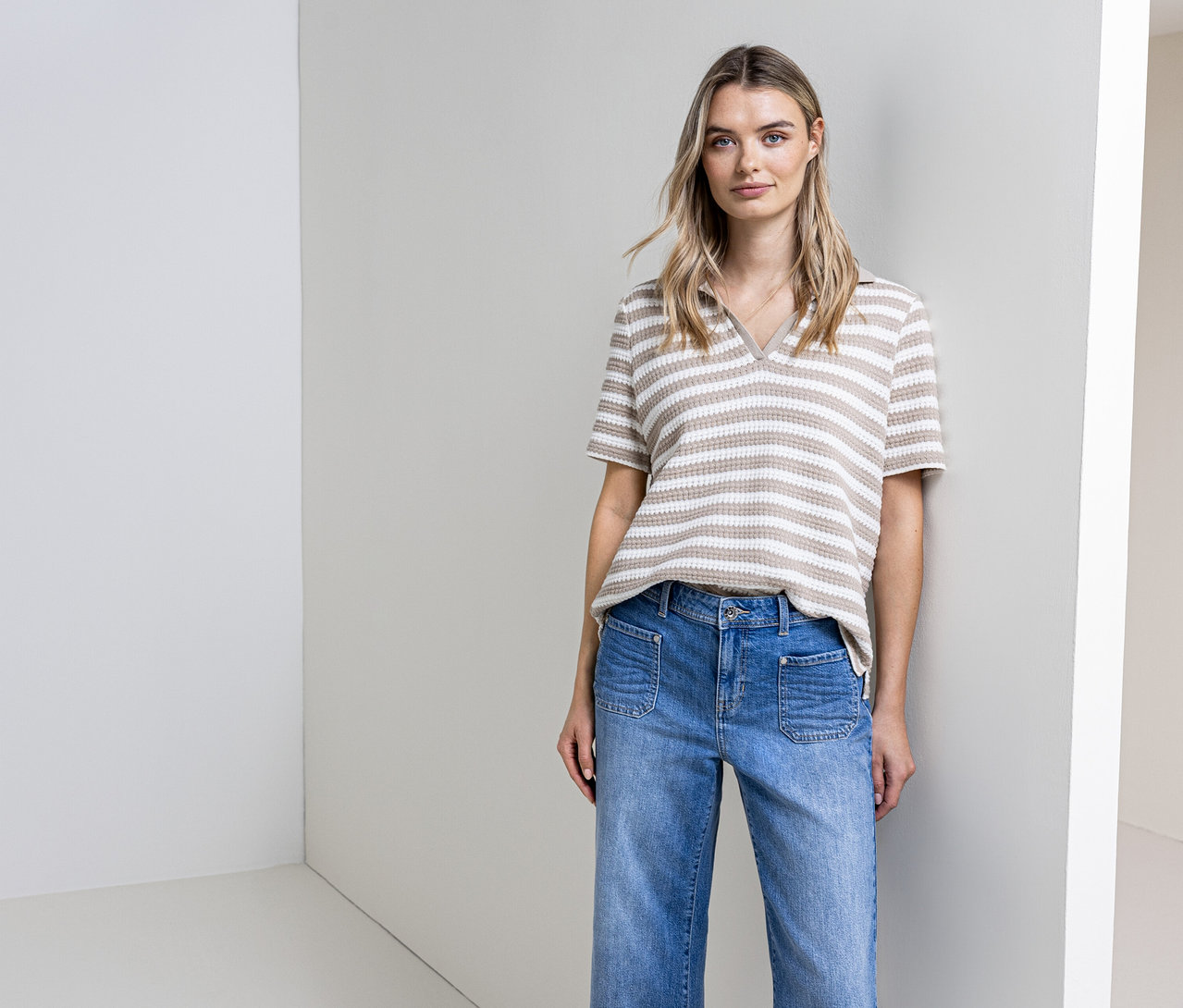Une femme pose en jean et pull en maille rayé Street One devant un mur.