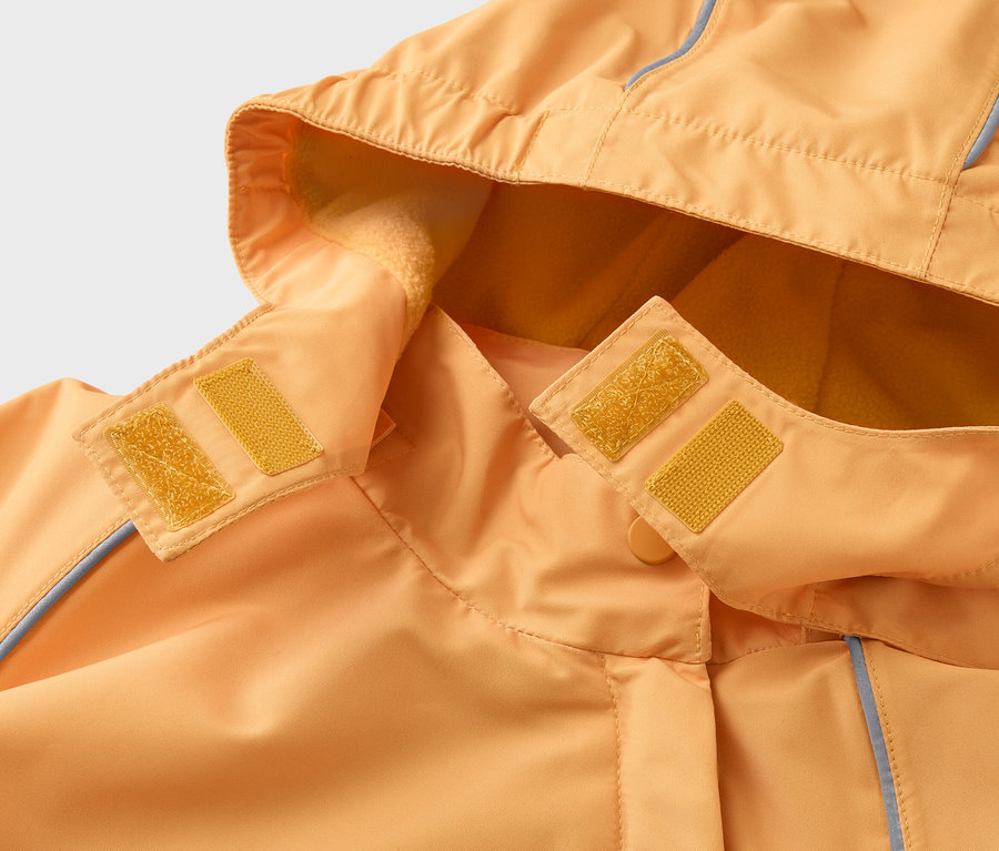 Gros plan sur une veste orange à capuche fixée par des scratchs jaunes. La capuche est doublée en polaire.