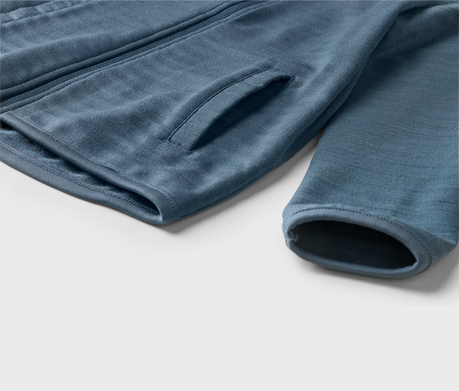 Gros plan d'une veste bleue montrant une fermeture éclair, une poche latérale et un poignet de manche.