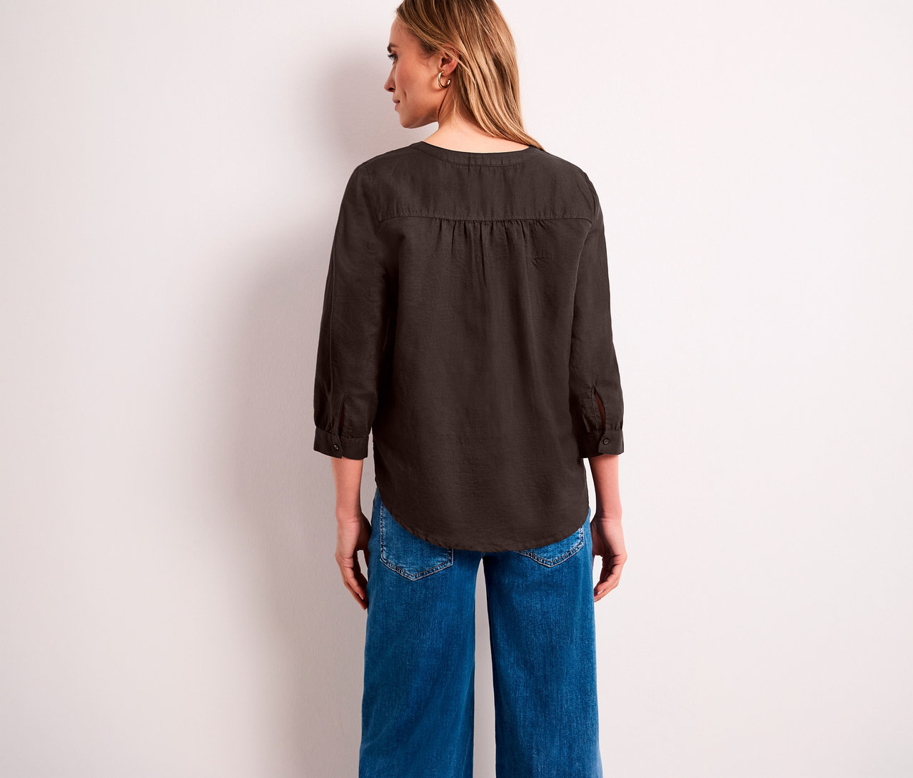 Une femme vue de dos, regardant vers la droite, porte une blouse-tunique Street One marron foncé à manches 3/4 et un jean large bleu.