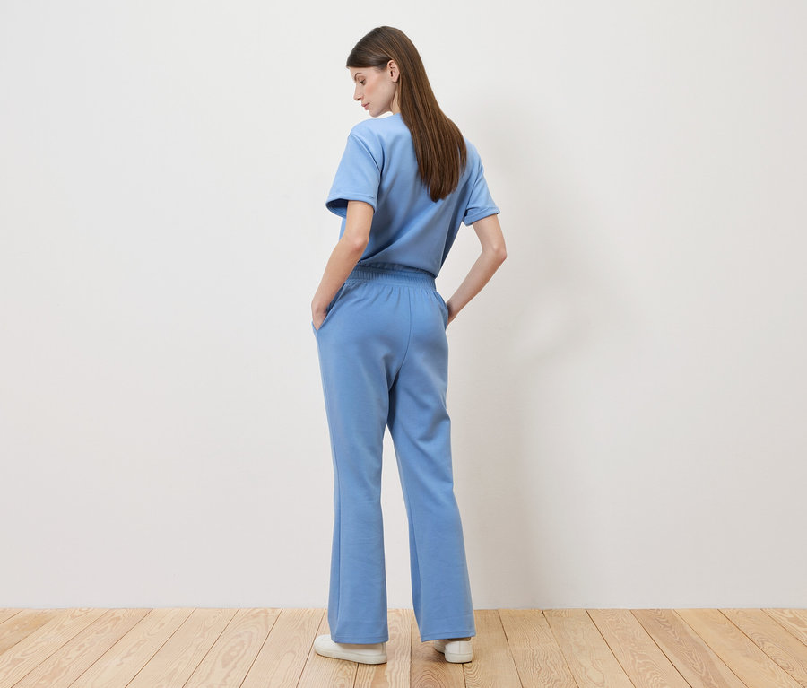 Femme debout dos à la caméra, portant un t-shirt bleu clair et un pantalon assorti