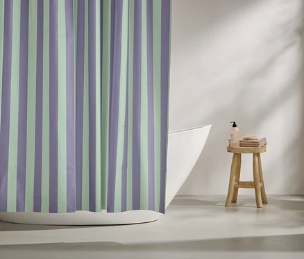 Un rideau de douche rayé violet et vert menthe est suspendu devant une baignoire. Des articles de toilette sont posés sur un tabouret.