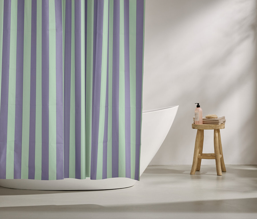 Un rideau de douche rayé violet et vert menthe est suspendu devant une baignoire. Des articles de toilette sont posés sur un tabouret.