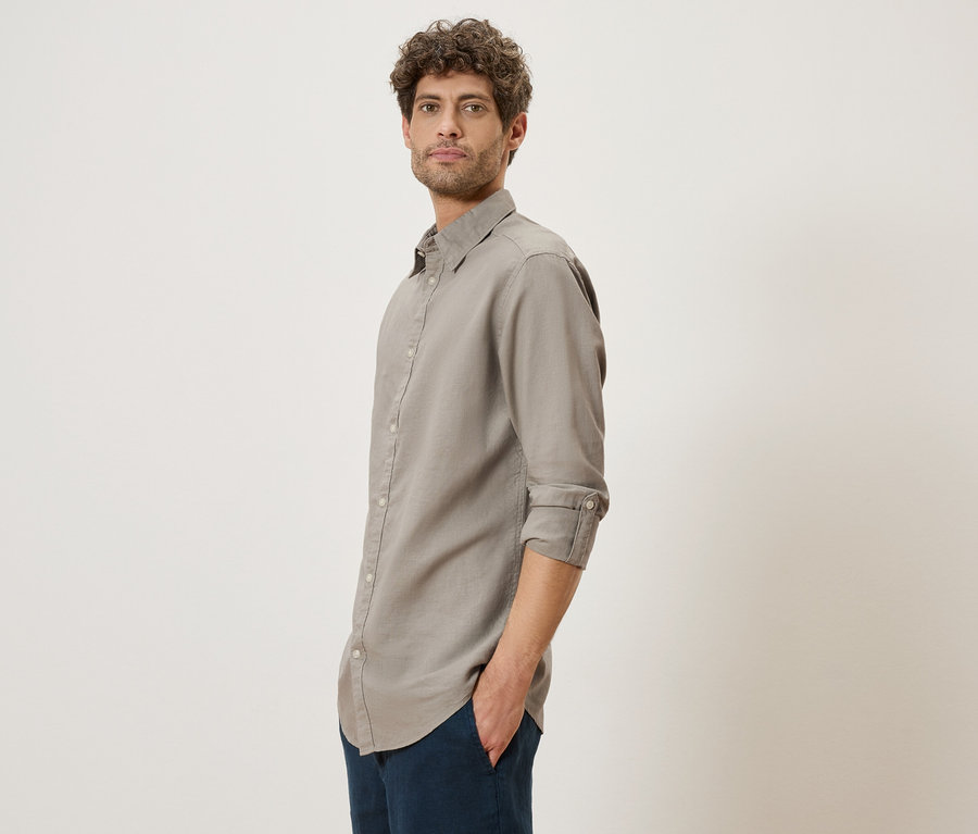 Homme aux cheveux bouclés portant une chemise grise à manches longues et un pantalon bleu marine.